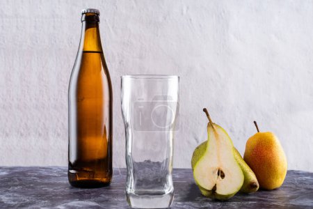 Empty glass near bottle and pear. A slice of pear and a glass. Front view.