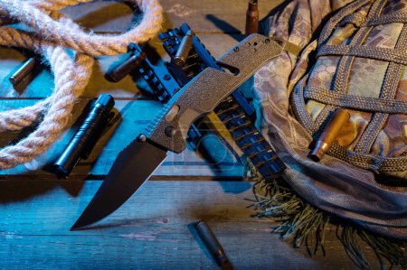 A folding knife with a green handle and a black blade. Military composition with a knife and bullets. Cold and warm light.