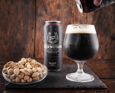 Photo for Kyiv, Ukraine - August 6, 2022: Cernovar dark beer in a glass and pistachios. Dark beer in a can. Pouring beer into a glass. Front view. - Royalty Free Image