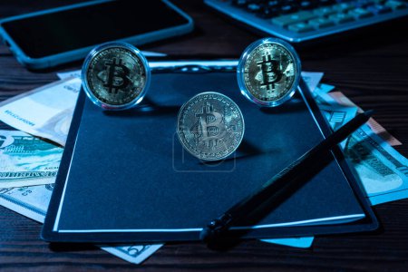 Foto de Varias monedas de bitcoin en una hoja negra. Bloc de notas negro y lápiz negro. Vista frontal. - Imagen libre de derechos