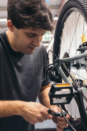 vertical portrait Caucasian bicycle mechanic adjusting chain with tool in workshop