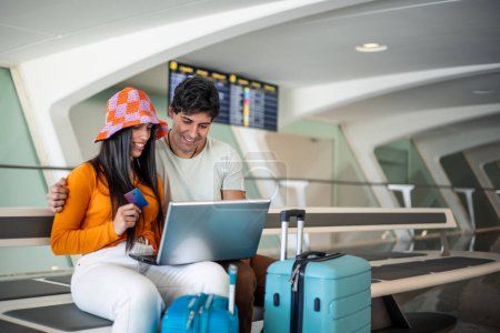 Foto de Pareja joven con tarjeta de crédito y computadora portátil que compra su vuelo en el aeropuerto con espacio para copias de equipaje - Imagen libre de derechos