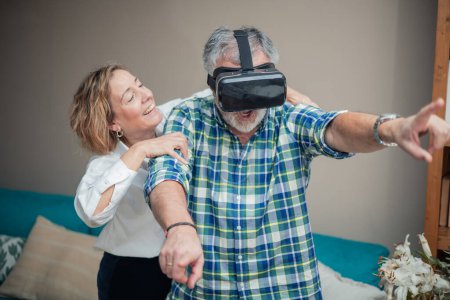 In the comfort of their living room, a senior couple dives into the realms of virtual reality. The man, adorned with VR glasses, wears a look of awe and excitement, his arms gesturing animatedly as he experiences the digital landscape. 