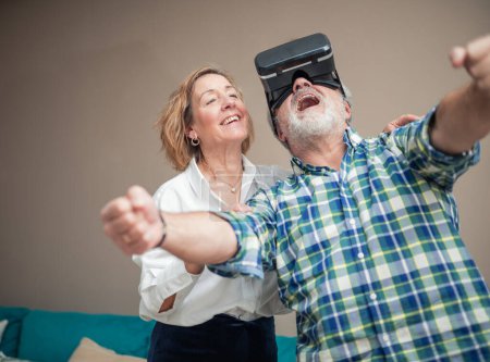 In their cozy living room, a senior couple embarks on a thrilling virtual reality journey. The man, wearing VR glasses, gazes upward with fascination and wonder, fully engrossed in the immersive digital experience unfolding before him. 