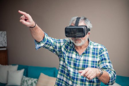 In seinem gemütlichen Wohnzimmer taucht ein Rentner in eine aufregende Virtual-Reality-Erfahrung ein. Mit der neuen VR-Brille hebt er die Hand in die Luft und navigiert mit Ehrfurcht und Neugier durch Anwendungen.. 