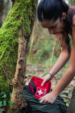 Photo for Vertical portrait A skilled bushcraft adventurer prepares for the challenges of the forest, deftly extracting a survival kit from her backpack. Her mastery of bushcraft is evident in her confidence and determination as she ventures into nature, ready - Royalty Free Image
