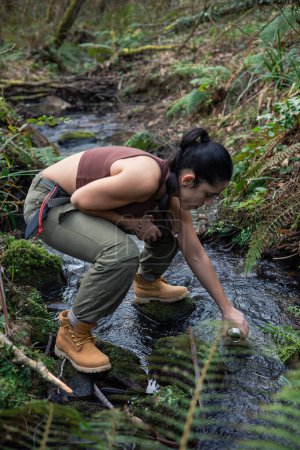 In this inspiring image, a brave adventurer immerses herself in nature to collect fresh water from a crystal-clear river. Her hands, infused with respect for the environment, capture the essence of sustainability and harmonious connection with nature