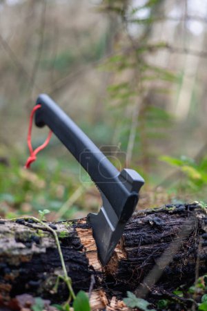 vertical portrait In this striking image, a bushcraft and survival axe stands proudly, firmly embedded in a tree trunk on the forest floor. This essential tool represents the skill and preparedness required to tackle the challenges of the wild. Its p