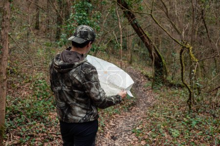 A man in camo, clutching a map, strides down a forest path, venturing into the untamed wilderness.