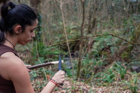 En un primer plano, una joven exploradora talla hábilmente con su cuchillo de supervivencia, encarnando la esencia de la artesanía salvaje