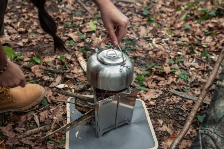 Nahaufnahme eines Metallkessels, der auf einem tragbaren Bushcraft-Herd auf dem Boden inmitten des Waldes steht und Outdoor-Abenteuer und Survival-Ausrüstung zeigt