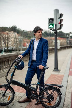 vertical portrait A young businessman confidently poses holding his electric folding bike and helmet in an urban setting. This image reflects his commitment to sustainable transportation and environmental care by choosing an eco-friendly mobility opt