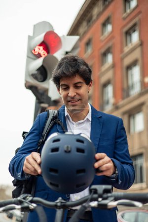 vertical portrait A businessman in a suit is seen preparing to ride safely with his electric bike in the city by putting on his helmet. This image highlights the importance of safety and eco-friendly transportation choices in urban environments
