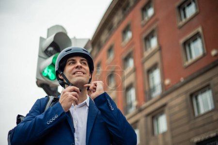 Um die Sicherheit zu gewährleisten, überprüft ein Geschäftsmann in offizieller Kleidung die Sicherheit seines Helms zweimal, bevor er sich auf eine urbane Radtour begibt. Dieses Bild unterstreicht die Bedeutung der Schutzausrüstung für umweltbewusste Pendler