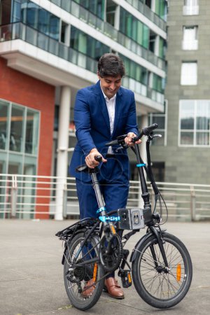 vertical portrait Male businessman wearing a blue suit is folding his electric folding bike in the bustling financial district of the city