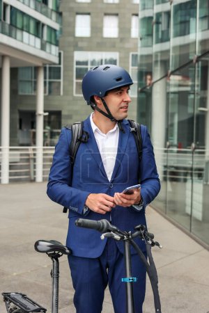 vertical portrait Male businessman wearing bike helmet and backpack standing next to his electric bicycle while holding smartphone