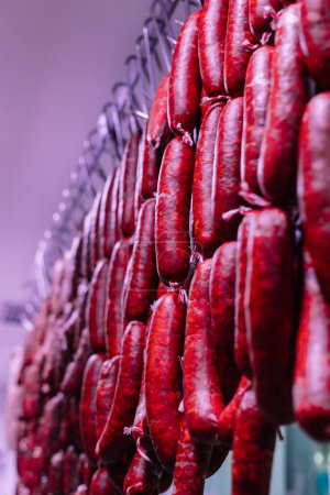 vertical portrait closeup of several strings of chorizo sausages hanging from the ceiling of the butcher shop, creating a picturesque and traditional scene