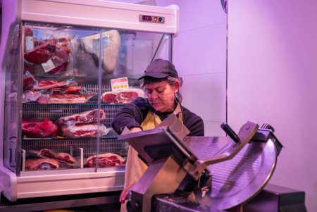 In this image, a female butcher is seen operating an electric meat slicer with intense focus and precision. The seamless motion of the machine, coupled with the skilled hands of the butcheress, highlights the expertise and dedication involved in the 