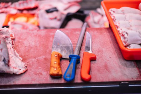 Foto de Primer plano dos cuchillos de carnicero y un afilador de cuchillos dispuestos en una tabla de cortar carne en una carnicería. Las herramientas son esenciales para la artesanía del carnicero, reflejando la precisión y la experiencia requeridas en la preparación de la carne. - Imagen libre de derechos