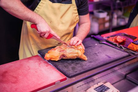 closeup of a butcher's hands wearing a yellow apron cutting chicken with a knife at the butcher shop counter, preparing it for a customer. The scene reflects the dedication and skill of the butcher in providing fresh and personalized products to thei