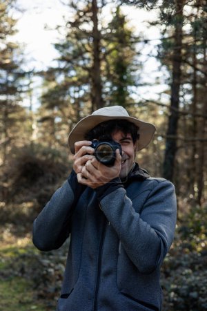 portrait vertical Un explorateur sauvage, revêtu d'un chapeau d'explorateur, se tient au milieu de la forêt luxuriante, concentrant son appareil photo pour documenter la beauté à couper le souffle de la générosité de la nature