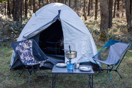Serene campsite nestled in nature featuring a tent, chairs, camping stove, and cooking utensils, offering the perfect outdoor getaway