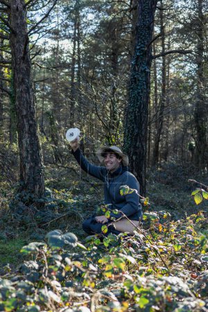 An explorer demonstrates environmental responsibility by attending to his needs behind bushes in remote nature, holding a roll of toilet paper in hand. This image underscores the importance of maintaining hygiene even during exploration in wild envir