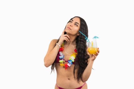thoughtful brunette Latin woman in a bikini holds a soda in her hand while contemplating, with her hand on her face, perhaps lost in thought or enjoying a warm beach day on white background