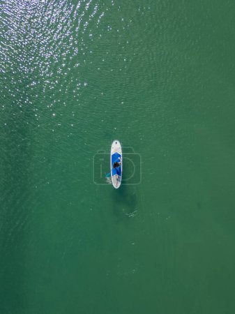 chica vista cenital vertical está remando con su paddleboard azul en el mar, disfrutando de un día sereno de deportes acuáticos y actividad al aire libre