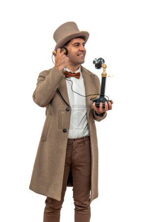 vertical, early 20th century vintage gentleman sporting a bowler hat and trench coat, as he makes a call using an antique English telephone. Experience the nostalgia as this classic scene