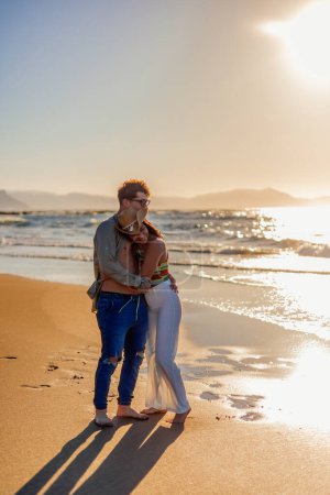 Téléchargez les photos : Couple hispanique embrasse affectueusement sur le rivage de la plage, silhouette contre le soleil couchant lors d'une soirée d'été. Leur étreinte aimante au milieu des teintes dorées du coucher de soleil vertical - en image libre de droit