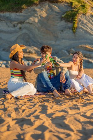Téléchargez les photos : Amis latins verticaux sur la plage profiter du coucher de soleil ensemble, élever leurs bouteilles de bière dans un toast à l'amitié et l'unité. Alors que le soleil plonge sous l'horizon, leur rire et leur camaraderie remplissent l'air - en image libre de droit