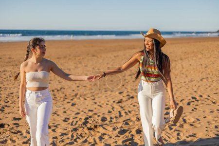 lateinisches multikulturelles lesbisches Paar geht Hand in Hand am Strand entlang, die Augen in einem Blick voller Liebe und Zuneigung verschlossen und feiert die Schönheit der Liebe in ihrer reinsten Form.