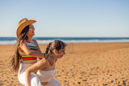 Multikulturelles Latina-lesbisches Paar reitet huckepack, lacht und schwelgt in seiner Liebe an einem sonnigen Sommertag am Strand, ein Beweis für die Schönheit der Liebe und Vielfalt