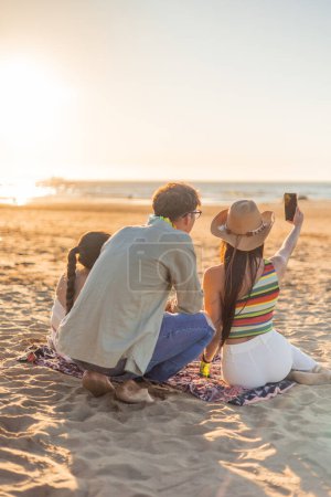 amigos multiculturales verticales se unen en la playa, capturando una selfie puesta de sol juntos. Contra el telón de fondo del fascinante horizonte, su camaradería brilla, creando recuerdos preciados