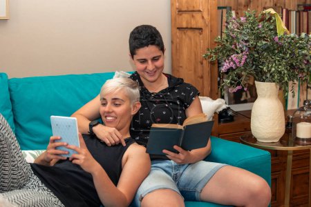 pareja de lesbianas relajarse en el sofá de la sala de estar, uno absorto en un libro electrónico, mientras que el otro disfruta de un libro de papel clásico, que simboliza la modernización de la literatura. Concepto de estilo de vida contemporáneo