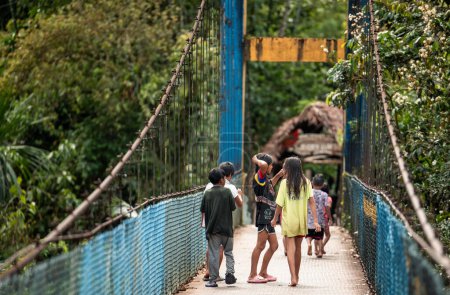 Eine Gruppe indigener Wayuri-Kinder überquert auf ihrem Weg in ihr Dorf in Ecuador eine Hängebrücke über den Puyo-Fluss. Dieses Bild fängt die kulturelle Essenz und das tägliche Leben des Stammes der Wayuri ein