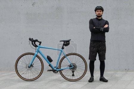 A cyclist in black cold weather clothing with a blue gravel bike on a concrete urban background.