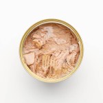 Canned tuna in oil, open tin on a white background.