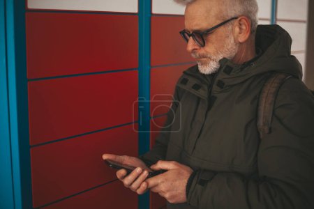Photo for Automatic parcel delivery machine. Mature man receives an online order in the mail terminal. - Royalty Free Image