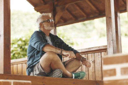 Téléchargez les photos : An elderly man with a beard sits on the terrace and thinks about life. Retirement and meditation. Age problems, feel young at heart. - en image libre de droit