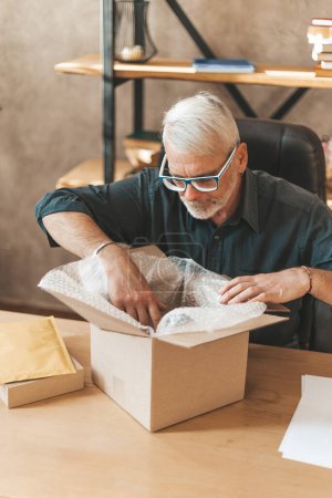 Photo for Damaged package. Disgruntled mature male shopper opens a box at home. Wrong delivery, return of goods. - Royalty Free Image