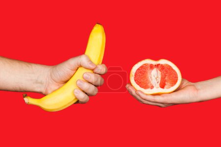 Téléchargez les photos : Erotic banana and donut in the hands as a symbol of the penis and vagina isolated on a red background. The relationship between a man and a woman, sex and passion. - en image libre de droit