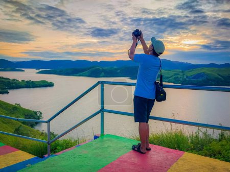 Téléchargez les photos : Un homme prend des photos au coucher du soleil sur la colline du lac Sentani, Jayapura, Papouasie - en image libre de droit