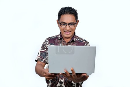 Ein indonesischer Mann trägt ein Batikhemd und arbeitet an einem Laptop