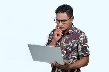 An Indonesian man wearing a batik shirt and working on a laptop