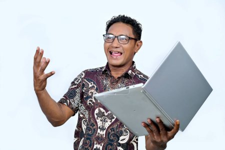 Ein indonesischer Mann trägt ein Batikhemd und arbeitet an einem Laptop