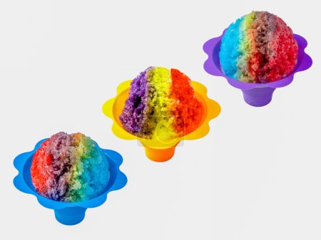 Three rainbow Hawaiian shave ice, shaved ice or snow cone desserts in a row against a white background