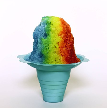 Hawaiian Rainbow Shaved ice, shave ice or a snow cone in a blue flower shaped cup against a white background.