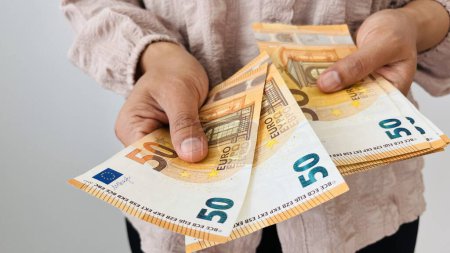 Eine Frau reicht zwei 50-Euro-Scheine und hält ein Bündel Eurogeld in der Hand. Euro-Scheine, Papierwährung der Europäischen Union. Sparkonzept. Finanzen, Unternehmen, Investitionen, Inflation, Kaufkraft